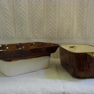 Pu&ograve; includere: Due fioriere rettangolari in ceramica. Una &egrave; marrone con base bianca, l'altra &egrave; marrone con interno color crema. Entrambe hanno una finitura lucida e sono poste su uno sfondo bianco strutturato.