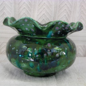 May include: A green ceramic bowl with a frilled rim. The bowl has a rounded base and a glossy finish with speckled accents in shades of pink and blue. The bowl is likely handmade and has a unique, artistic appearance.