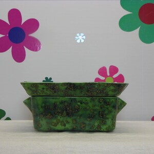 May include: A rectangular ceramic baking dish with two side handles, featuring a vibrant green glaze with dark brown speckled accents throughout the surface. The dish is composed of two stacked pieces, a shallow lid and a deeper base container.