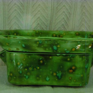 May include: A two-piece ceramic serving dish set. The set includes a rectangular base with handles and a matching, slightly larger, rectangular top. The dishes are glazed in a speckled green with accents of yellow and teal.