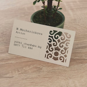 May include: A white business card with black text and a decorative design. The text reads "N. Mecherinkova Artist" and "yukki_chan@abv.bg 0877 713 884".