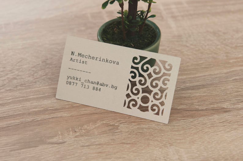 May include: A white business card with black text and a decorative design. The text reads "N. Mecherinkova Artist" and "yukki_chan@abv.bg 0877 713 884".