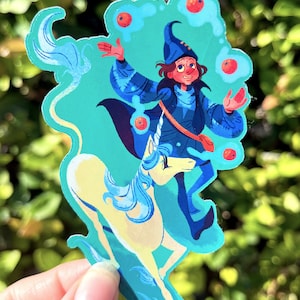 May include: A whimsical sticker featuring a wizard in blue robes and hat, juggling red orbs while riding a yellow unicorn with a flowing blue mane. The sticker has a teal background and a unique shape.