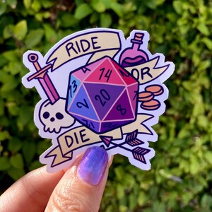 May include: A sticker featuring a multi-colored 20-sided die with the numbers 13, 2, 20, 7, 14, and 8. The die is surrounded by a sword, a skull, a potion bottle, two gold coins, and a banner that reads "Ride or Die".