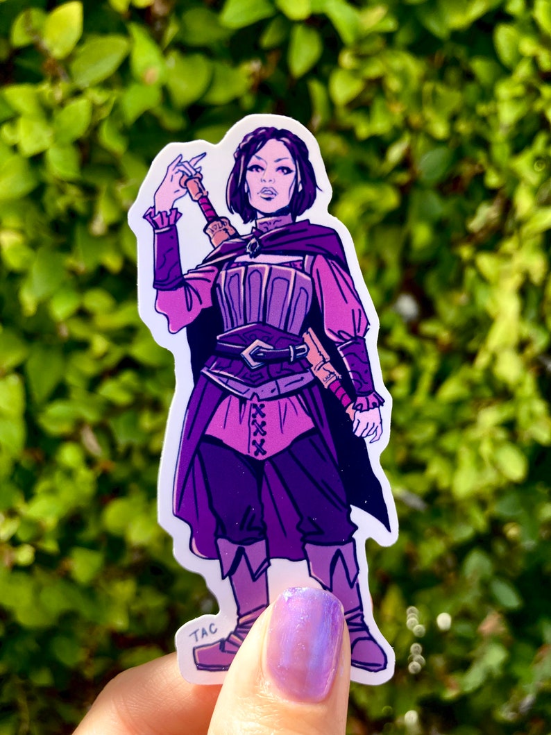 Puede incluir: Una pegatina morada y rosa de un personaje femenino con el pelo corto y oscuro, que lleva un atuendo morado y rosa y sostiene una espada. La pegatina tiene el texto "TAC" en la esquina inferior izquierda.