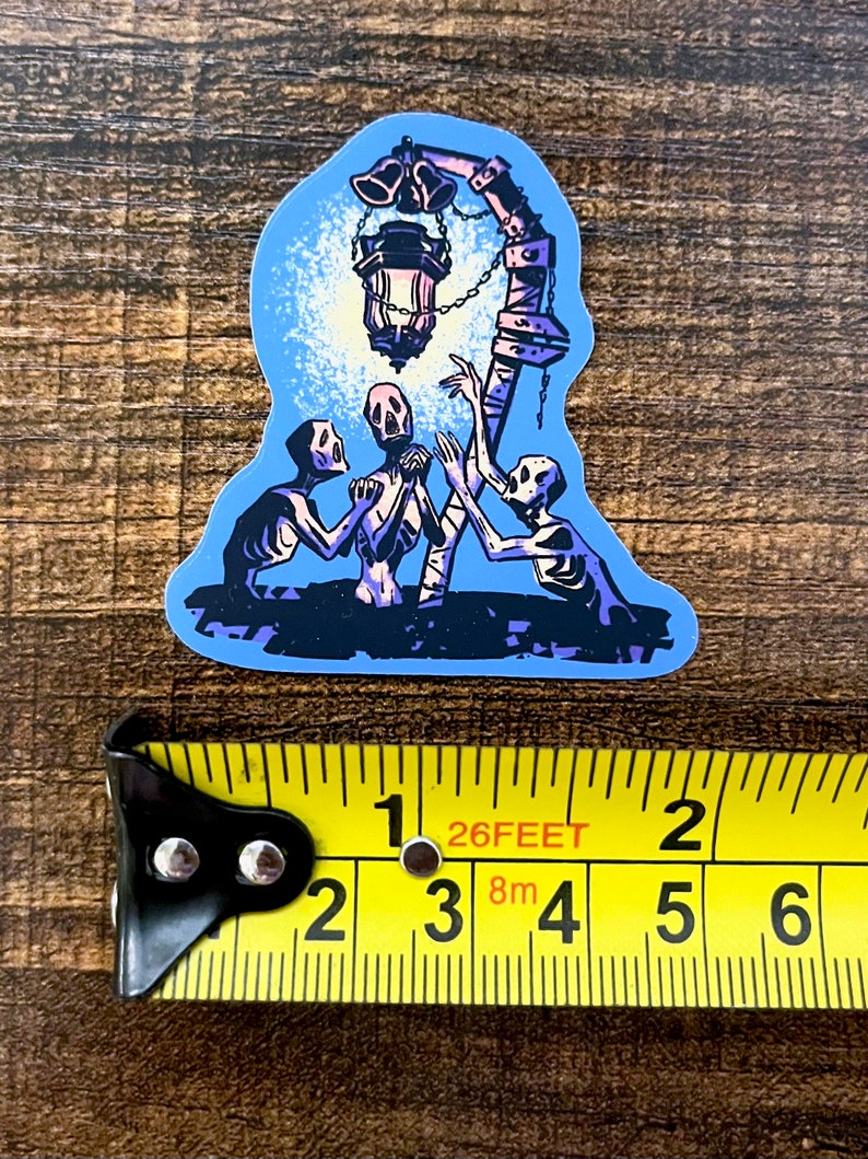Pu&ograve; includere: Un adesivo con un'illustrazione blu e viola di tre scheletri che raggiungono una lanterna appesa a un palo con delle campane. La lanterna &egrave; accesa e proietta un bagliore sugli scheletri.