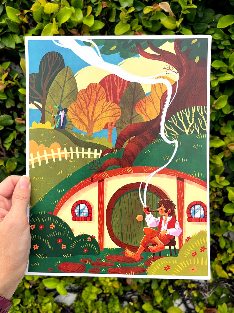 Op de afbeelding: Een kleurrijke illustratie van een hobbit die buiten een ronde deur zit met een pijp in zijn mond. De hobbit draagt een bruin vest en broek. De deur is groen met een messing handvat. Er is een wit hek op de achtergrond en een klein figuur in de verte.