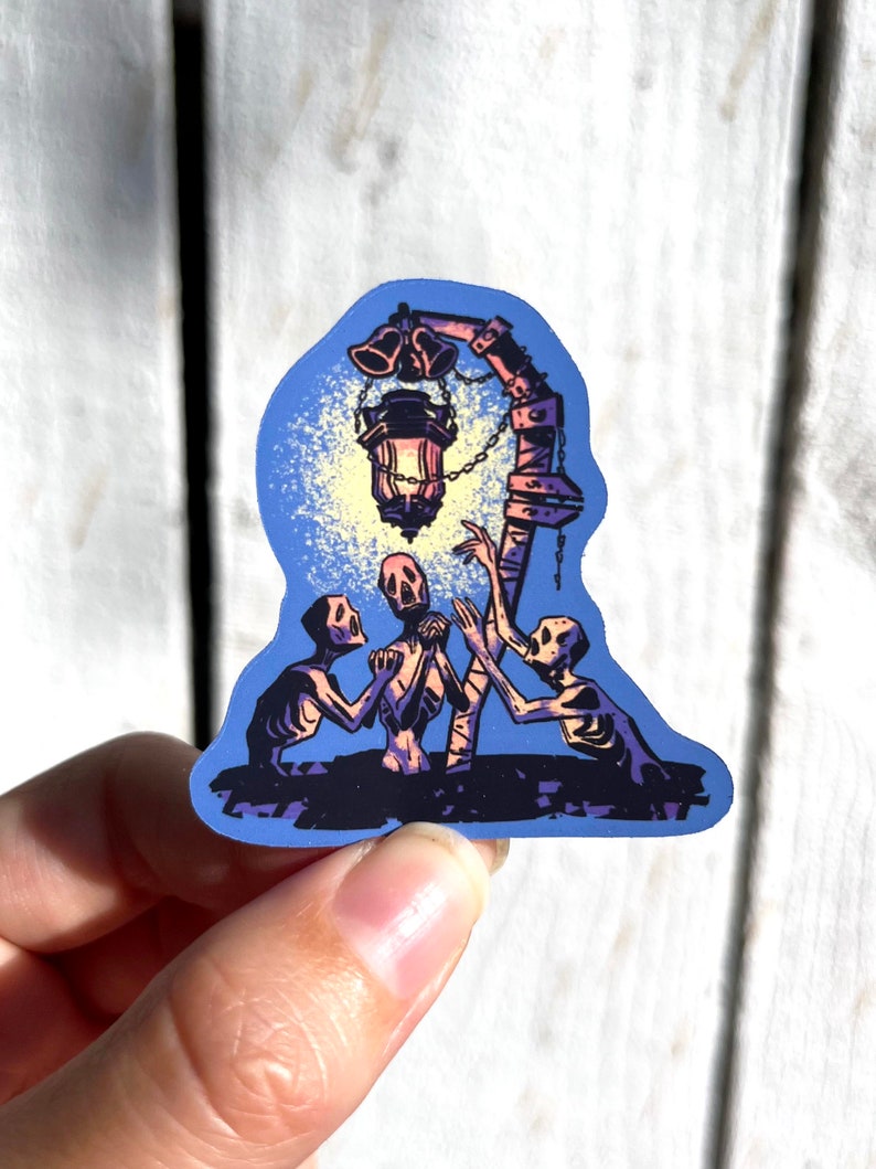 Pu&ograve; includere: Un adesivo con un'illustrazione blu e viola di tre figure scheletriche che raggiungono una lanterna incandescente appesa a un palo di legno.