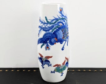 May include: White ceramic vase featuring a blue and red phoenix design. The vase is tall and slender with a rounded base.