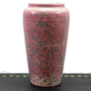 May include: A tall, pink ceramic vase with a speckled green glaze. The vase has a rounded bottom and a slightly flared opening.