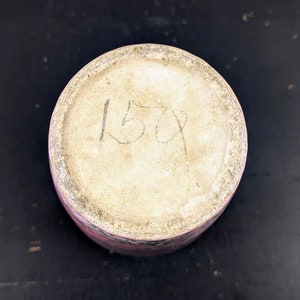 Może przedstawiać: Sp&oacute;d r&oacute;żowego wazonu ceramicznego z białym wnętrzem. Na spodzie wazonu napisane jest czarnym atramentem 1509.