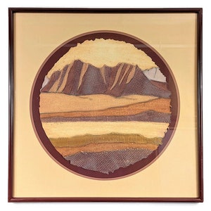 May include: A framed artwork featuring a circular collage of textured paper in shades of brown, beige, and gold, depicting a mountain range.