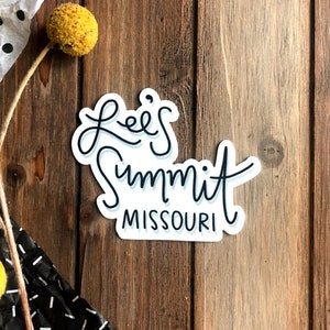 Op de afbeelding: Witte sticker met zwarte tekst in cursief schrift die "Lee's Summit Missouri" luidt.
