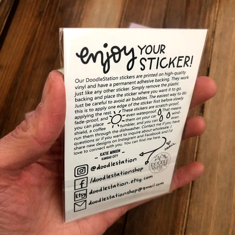 May include: A white card with black text explaining how to use and care for DoodleStation stickers. The card includes a sun, raindrop, and wind icon. The text includes the social media handles @doodlestation and doodlestationshop.etsy.com.