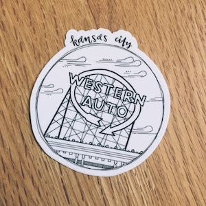 Op de afbeelding: Zwart-witte illustratie van het Western Auto-bord in Kansas City, Missouri. Het bord is een grote, ronde structuur met een ontwerp dat lijkt op een reuzenrad. De woorden "Western Auto" zijn geschreven in een vet, gestileerd lettertype.