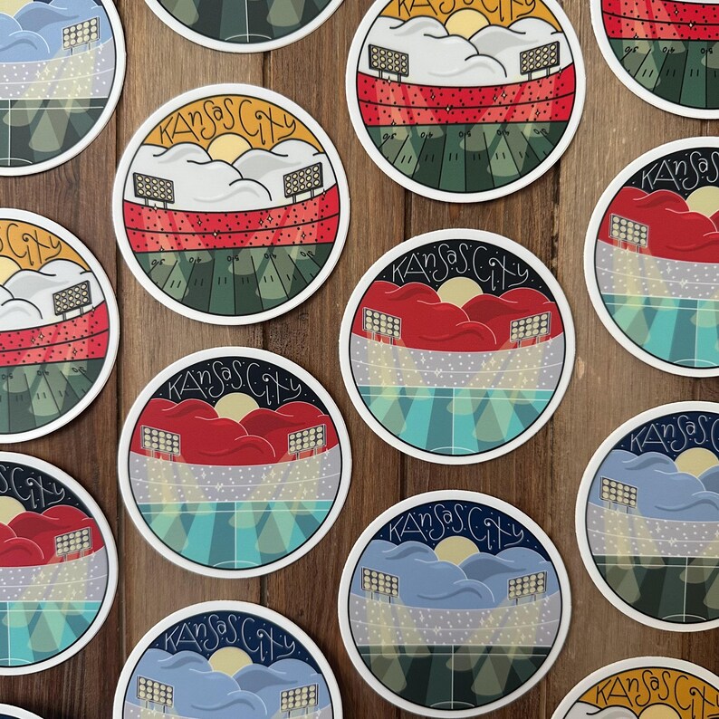 May include: A collection of round stickers featuring a stadium design with the text "Kansas City". The stickers have a white border and depict a stadium with a sunset, clouds, and various color schemes, including red, blue, and green.
