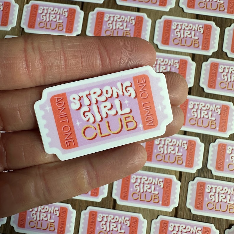 May include: Pink and orange ticket-shaped sticker with the text "Strong Girl Club" and "Admit One" on it.