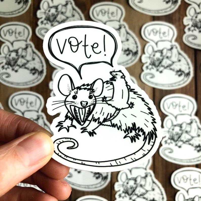 May include: A black and white sticker featuring a cartoon rat with a smaller rat riding on its back. The larger rat has a toothy grin and the sticker has the word "Vote!" in a speech bubble above the rats.