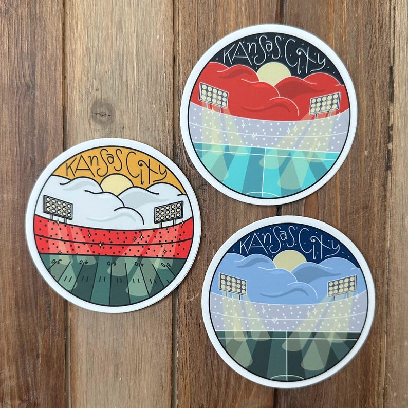 May include: Three round stickers with a Kansas City theme. Each sticker features a stadium design with the words "Kansas City" in a curved font at the top. The stadium designs have different color schemes, including red, blue, and yellow.