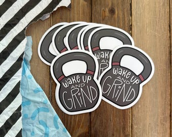 May include: A set of six white stickers with a black and grey kettlebell design. The stickers feature the text "Wake Up and Grind".