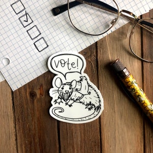 May include: A black and white sticker of a rat with a smaller rat on its back. The rat is holding a sign that says "Vote!"