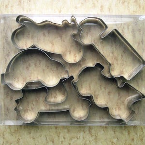 May include: A set of six metal cookie cutters shaped like different vehicles, including a car, a truck, a motorcycle, and a scooter. The cutters are packaged in a clear plastic container.