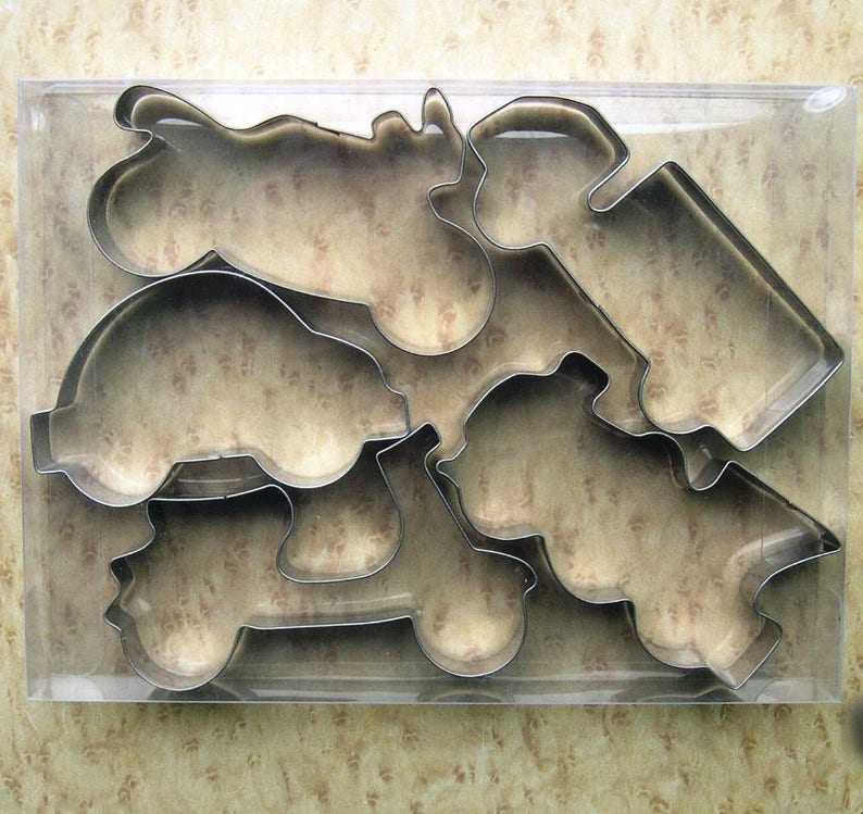 May include: A set of six metal cookie cutters shaped like different vehicles, including a car, a truck, a motorcycle, and a scooter. The cutters are packaged in a clear plastic container.