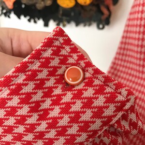 May include: Red and white houndstooth fabric with a white button with an orange center.