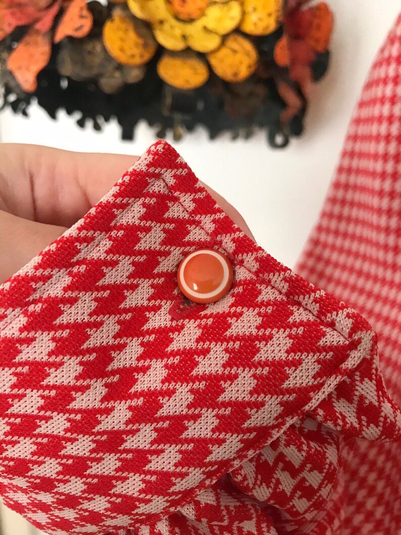 May include: Red and white houndstooth fabric with a white button with an orange center.