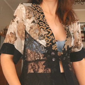 May include: A black and white floral patterned kimono with a gold and black patterned trim. The kimono has a lace overlay and a black fabric underneath. The kimono has a deep V-neckline and is open in the front.