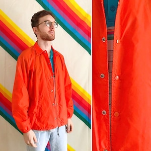 May include: A bright orange jacket with a snap closure and a drawstring waist. The jacket is made of a lightweight material and has a casual style.