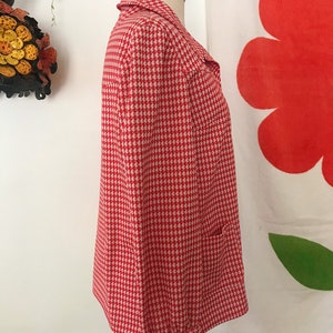 May include: A red and white houndstooth patterned long-sleeve shirt with a button-up front and a single pocket on the left side.