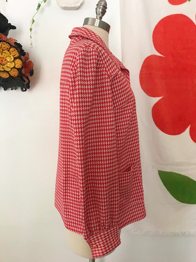 May include: A red and white houndstooth patterned long-sleeve shirt with a button-up front and a single pocket on the left side.