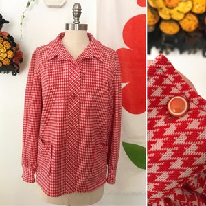 May include: A red and white houndstooth patterned button-up shirt with long sleeves and two pockets. The shirt has a collared neckline and is made of a lightweight fabric.