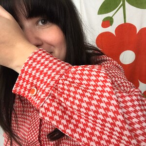 May include: A red and white houndstooth patterned blouse with a button on the cuff.