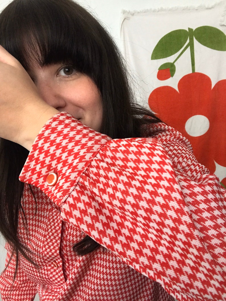 May include: A red and white houndstooth patterned blouse with a button on the cuff.