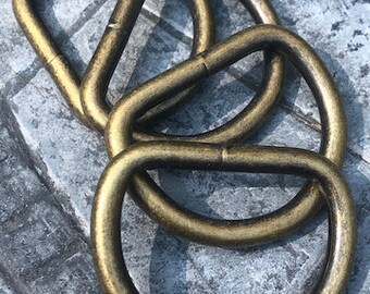 May include: Four gold-colored metal D-rings stacked on top of each other. The rings are smooth and have a slightly worn finish.