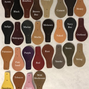 May include: A collection of 25 leather labels with various colors and names, including Acorn, Bourbon, Celery, Fudge, Honey, Cement, Indigo, Marine, Molasses, Navy Buc, Mahogany, Mocha, Naked, Oxblood, Palomino, Pink Sand, Tobacco, Sunshine, Purple, Violet, Rust, Storm, String, Smoke, Red, and Wild Mushroom.