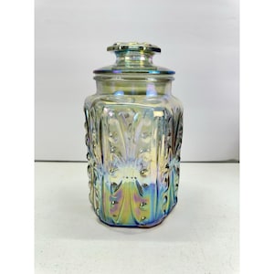 May include: A glass canister with a removable lid, featuring an iridescent finish that shifts between gold, blue, and purple hues. The exterior surface is decorated with a repeating pattern of vertical raised ridges and small circular dots.