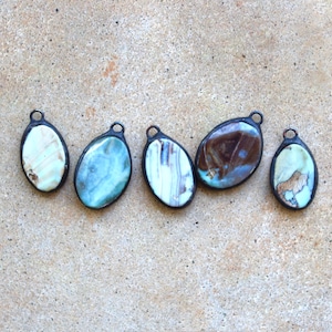 May include: Five oval-shaped pendants with a dark metal border. The pendants feature a variety of colors, including light blue, brown, and white, with unique patterns. Each pendant has a small loop at the top for hanging.