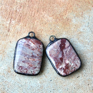 May include: Two rectangular pendants with a black metal frame and a red, white, and brown marbled stone inlay.