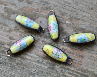May include: Five yellow ceramic beads with floral designs and black metal accents. Each bead has a loop at the top for attaching to a necklace or bracelet.