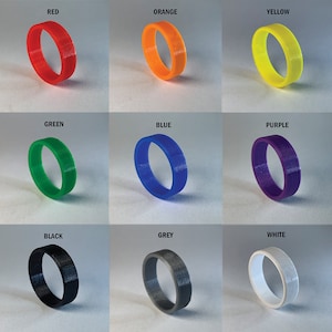May include: A set of 12 silicone rings in various colors, including red, orange, yellow, green, blue, purple, black, grey, and white. The rings are all the same size and shape, and they are arranged in a grid pattern.