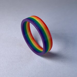 May include: A rainbow-colored silicone ring with a purple base. The ring is made of multiple layers of silicone, each a different color of the rainbow.