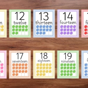 May include: Ten flashcards with numbers eleven through twenty. Each card has a number, the word form, and a ten frame with colored circles. The cards have a gingham border in various pastel colors, perfect for educational use.
