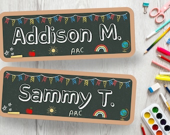 May include: Two chalkboard style name tags with a brown border. The top tag says "Addison M." and the bottom tag says "Sammy T." Both tags have a string of colorful flags, a sun, a rainbow, an apple, and a globe drawn on them.