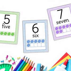 May include: Educational flashcards with numbers 5, 6, and 7, each with the number, word, and a ten-frame representation. The cards have a gingham border in green, blue, and purple. School supplies like pencils, a ruler, and glue are in the foreground.
