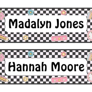 May include: Two name tags with a black and white checkered border. Each tag has a white center with a name in bold black letters. Decorative elements include a pencil, apple, flowers, rainbow, and clock.