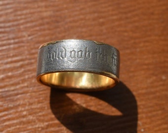 May include: A silver band with a gold inner band and an inscription in a gothic font that reads "And God said it is good".