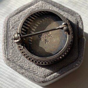 K&ouml;nnte beinhalten: Eine silberne Brosche mit einem runden, filigranen Design. Die R&uuml;ckseite der Brosche tr&auml;gt die Worte "Depose Sterling" und einen Stern.